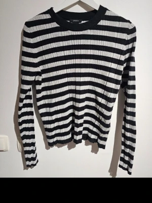 Randig ribbad tröja från Uniqlo - Säljer en svartvit ribbad tröja från Uniqlo med horisontella ränder. Tröjan har rund halsringning och långa ärmar. Materialet är stretchigt och sitter snyggt på kroppen. Perfekt för dig som gillar en enkel men stilren look.