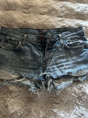 Ljusblåa jeansshorts från Replay - Säljer ett par ljusblåa jeansshorts från Replay med slitna detaljer och fransig kant. Köpte de här på plock men va för små för mig. 