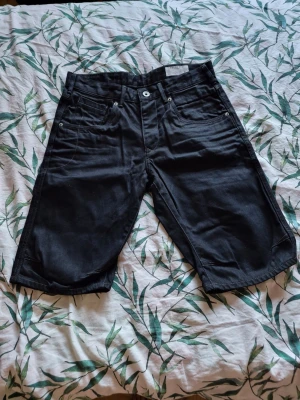 Svarta loose shorts i denim - Svarta denimshorts med fem fickor och längre ben, loose fit och klassisk jeanslook. Perfekta för en avslappnad stil och har bälteshällor samt knapp- och dragkedjestängning framtill.