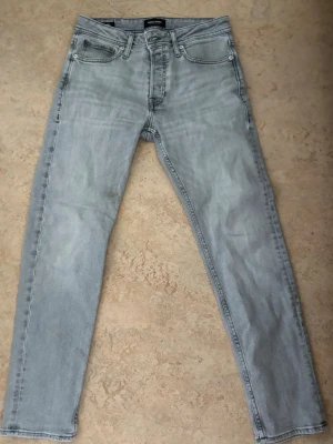 Ljusgrå slim fit jeans från Jack & Jones - Snygga ljusgrå slim fit jeans från Jack & Jones med klassisk femficksdesign och diskreta sömmar på bakfickorna. Jeansen har dragkedjegylf och är tillverkade i mjuk denim med lite stretch för extra komfort.