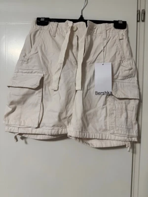Cargo shorts - Stilrena beiga cargo shorts från Bershka med flera stora fickor på sidorna och snörning i midjan.  Aldrig använda, prislapp kvar.