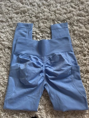 Ljusblå scrunch leggings med fickor - Säljer ett par ljusblå leggings med scrunch-detalj bak och bred ribbad midja. Leggingsen har praktiska sidofickor och är stretchiga och bekväma med snygg passform. Aldrig använda då de var för korta på mig som är 175💞