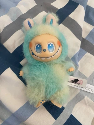 LABOBO TheMonsters blågrön mjukisdocka - Helt ny Söt LABOBO från TheMonsters med fluffig blågrön pälsdräkt och kaninöron. Dockan har stort leende, blå ögon och runda kinder. Tillverkad i mjukt syntetmaterial och har en etikett på sidan. Perfekt som samlarfigur eller dekoration.Nypris 999:-