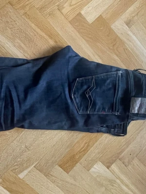 Replay jeans, Dondups, Replays - Säljer ett par mörkblåa jeans från Replay i storlek 32/34med klassisk femficksdesign och snygga kontrastsömmar på bakfickan. Jeansen har en skinnpatch med Replay-logga i midjan och är tillverkade i stretchigt denimtyg för extra komfort.