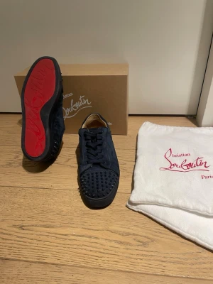 Mörkblå Louboutins med spikar bak och fram - Louboutin seavaste 2 orlato flat i bra skick plus box och skorpåsarna, har tagits hand om väll. Skorna är perfekt skick förutom en defekt som är att vänster sko har tappat en av front spikarna.