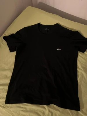 Svart t-shirt från BOSS - Snygg svart t-shirt från BOSS med diskret logga i vitt på bröstet. Klassisk rund halsringning och korta ärmar. Tillverkad i mjukt material som känns skönt mot huden. Perfekt basplagg för en stilren look.