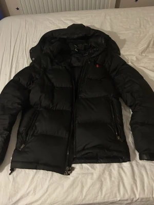 Svart pufferjacka från Polo Ralph Lauren - Säljer en svart pufferjacka från Polo Ralph Lauren med huva och två dragkedjeförsedda fickor. PRIS KAN DISKUTERAS!