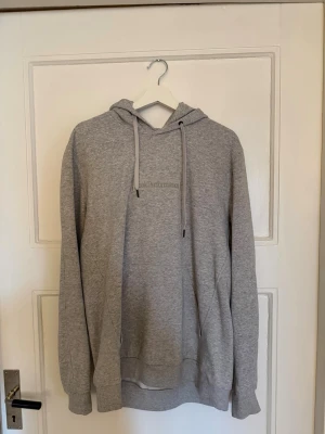 Grå hoodie peak performance  - Snygg grå hoodie från peak performance med broderad logga på bröstet. Klassisk modell med huva och dragsnören samt ribbade muddar vid ärmar och nederkant. Tillverkad i mjuk bomullsblandning som känns skön mot huden. Perfekt för en avslappnad och stilren look.