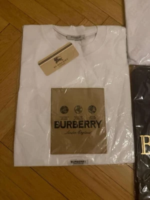 Vit Burberry t-shirt med tryck - Säljer en vit t-shirt från Burberry med klassiskt tryck på bröstet i beige och svart.  Finns i storlek L också
