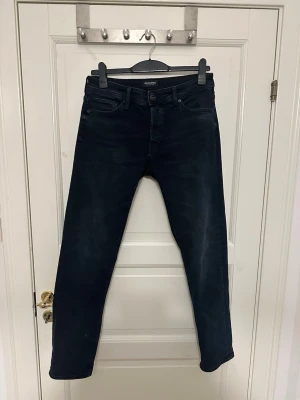 Svarta/blå jeans från Jack & Jones - Snygga svarta/blå jeans från Jack & Jones med klassisk femficksmodell och raka ben. Jeansen har en diskret tvättad look och är tillverkade i mjukt denimtyg med stretch för extra komfort. Perfekta för en avslappnad och stilren outfit. Storlek 31/32