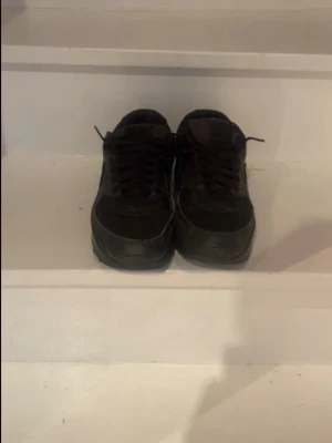 Svarta Nike Air Max sneakers - Säljer ett par helsvarta Nike Air Max sneakers med klassisk siluett och synlig luftbubbla i sulan. Skorna har en låg profil, snörning och är tillverkade i en mix av läder och textil. Perfekta för dig som gillar streetwear och sportig stil. Storlek 43 