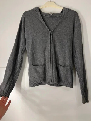 Finstickad kofta - Lindex - Mysig grå hoodie med dragkedja framtill och två fickor. Tröjan har långa ärmar, ribbade muddar och en skön huva. Perfekt för lager på lager och chill dagar. Materialet känns mjukt och stretchigt.