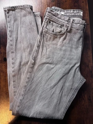 Grå raka jeans från Jack & Jones - Säljer ett par grå jeans från Jack & Jones med rak passform och klassisk femficksdesign. Jeansen har en snygg tvättad look och är gjorda i bomull. Perfekta till en avslappnad stil och passar till det mesta i garderoben.