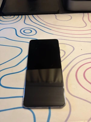 Samsung Galaxy S21 svart - Snygg Samsung Galaxy S21 i svart med stilren design och rundade hörn. Telefonen har en stor skärm och baksidan är i matt material med tre kameror och LED-blixt. Perfekt för dig som vill ha en kraftfull Android-mobil med modern look.