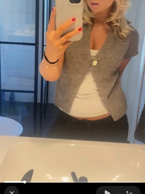 Grå kortärmad stickad kofta - Säljer en grå, kortärmad stickad kofta med en knapp framtill. Koftan har en avslappnad passform och är perfekt att slänga över ett linne eller t-shirt. Enkel och stilren design som passar till mycket.