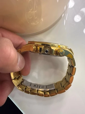 Guldfärgad klocka från BOSS - Stilren guldfärgad klocka från BOSS med blå urtavla och tre mindre subdials. Länken är i metall och har en klassisk design. Klockan har tydliga markeringar och detaljer i guld, vilket ger en lyxig känsla.