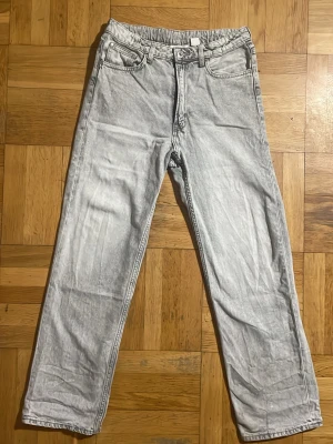 Ljusgrå raka jeans med tvättad look - Säljer ett par ljusgrå jeans med rak passform och klassisk femficksdesign. Jeansen har en snygg tvättad effekt och normal midja. Perfekta för en avslappnad och trendig stil. Materialet är denim i bomull.
