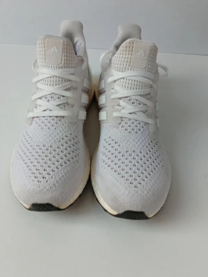 Vita Adidas Ultraboost sneakers - Snygga vita Adidas Ultraboost sneakers med stickad ovandel i mesh för extra andningsförmåga. Klassiska tre ränder på sidan och bekväm Boost-sula. Perfekta för dig som gillar stilrena och sportiga skor. Skorna har vita snören och diskret Adidas-logga på plösen.