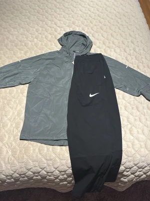 Hela nike dressen för bara 700 kr !! - Snygg grå vindjacka från Nike med huva och dragkedja framtill. Jackan har diskret Nike-logga på bröstet och är tillverkad i lätt, vindtätt material. Perfekt för blåsiga dagar och enkel att matcha med olika outfits.