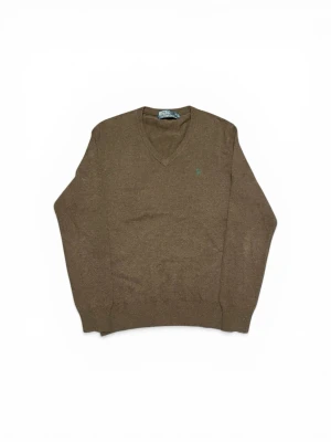 Brun v-ringad tröja Polo Ralph Lauren - Brun v-ringad tröja från Polo Ralph Lauren med diskret broderad logotyp i grönt på bröstet. Tröjan har långa ärmar och ribbade muddar vid ärmslut och nederkant. Perfekt för lager-på-lager och enkel att matcha med jeans.