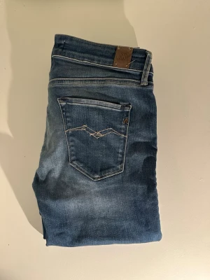 Blå slim jeans från replay - Säljer ett par blå slim jeans från replay med klassisk femficksdesign och snygga slitningar framtill. Jeansen har en ljus tvätt och smal passform som sitter tajt längs benen. Perfekta till en avslappnad och trendig look.