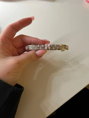 Hårspänne med rosa rosett och pärlor - Säljer ett gulligt hårspänne i metall med dekorationer av små vita pärlor och en söt rosa rosett i mitten. Spännet har även rosa detaljer på sidorna och ger en riktigt söt och feminin look. Perfekt för att piffa till frisyren med lite extra bling✨🥰 vi är ett UF företag som designar hårspännen och gör skedspännen🤗🤍