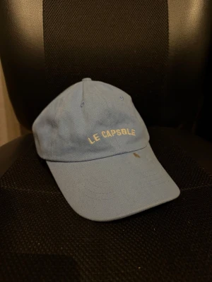 Ljusblå keps från Le Capsule storlek one size - Snygg ljusblå keps från Le Capsule med broderad text framtill. Klassisk böjd skärm och justerbart spänne bak. Tillverkad i bomullstyg som ger en avslappnad vibe. Perfekt accessoar för att lyfta din streetstyle.