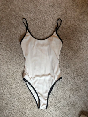 Svartvit body - Säljer en vit ribbad bodysuit med tunna axelband och svarta kontrastkanter. Sitter tight och har en enkel, stilren look som passar perfekt till jeans eller kjol. Materialet känns mjukt och stretchigt, vilket gör den bekväm att bära hela dagen. Jättebra skick och sitter så fint på kroppen❤️❤️