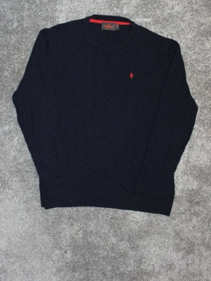 Mörkblå kabelstickad tröja Polo Ralph Lauren - Mörkblå kabelstickad tröja från Morris med röd broderad logga på bröstet. Tröjan har rund halsringning och ribbade muddar vid ärmslut och nederkant. Perfekt för lager på lager och klassisk stil. Modellen är 181 och bär vanligtvis S/M🌟 hör gärna av dig med frågor‼️