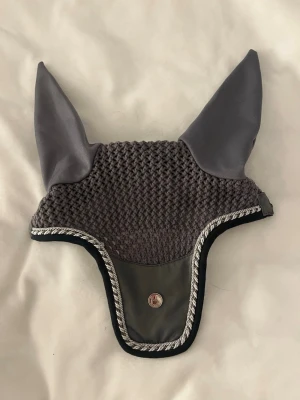 Grå huva från PS of Sweden - Snygg grå huva från PS of Sweden med stickad ovandel och släta tygöron. Dekorativ kant i vitt och grått samt en metallbricka med PS-logga framtill. Perfekt accessoar för häst och ridning.