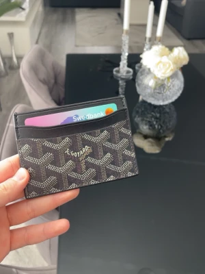 Svart stilren korthållare - Svart korthållare i stilren design. Smidig och kompakt, perfekt för dig som vill ha det viktigaste nära till hands utan en klumpig plånbok. Har flera fack för kort och funkar lika bra till vardags som till finare tillfällen. Väldigt lite använd och i fint skick.