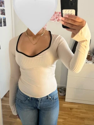 Ribbad beige långärmad topp med svart kant - Fin topp i beige med lång ärm och snygg v-ringning som ramas in av en svart kant. Figurnära passform, perfekt till jeans eller kjol. Enkel men ändå unik detalj med kontrastfärgad kant. Endast använd några gånger.