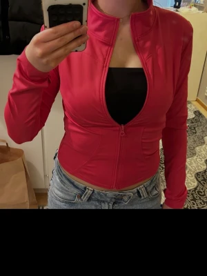 Rosa träningsjacka - Snygg rosa träningsjacka med lång ärm och dragkedja framtill. Figurnära passform som framhäver midjan. 