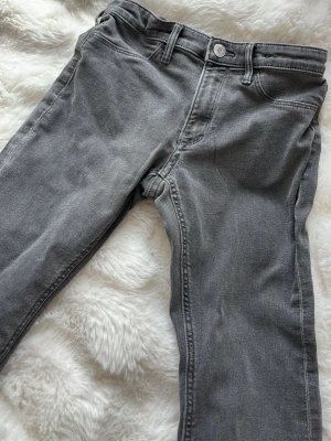 Grå bootcut jeans - Snygga grå jeans med bootcut-modell och hög midja. Klassisk femficksdesign och bälteshällor. Jeansen har en avslappnad passform och är tillverkade i mjukt denimtyg. Perfekta för en trendig och avslappnad look.