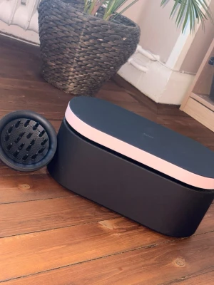 Rosa och svart hårfön med tillbehör - Säljer en snygg hårfön från dyson. Hårfönen är metallicrosa med ljusrosa detaljer, Kommer i en svart oval förvaringsbox med rosa lock och flera munstycken, inklusive en diffuser. ( alla delar ingår i detta köp) Den är helt ny och har bara använts 2 gånger. perfekt för styling eller hår torkning. Kvitto finns, det är bara o fråga💕