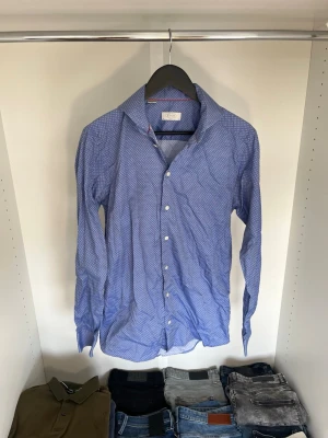 Blå mönstrad skjorta från Eton - Snygg blå skjorta från Eton med diskret mönster och klassisk krage. Skjortan har lång ärm och vita knappar framtill. Hör gärna av dig vid frågor!