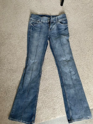 Blå bootcut jeans med rand - Ett par blå bootcut jeans med pressveck längs benen. Jeansen har låg midja och stängs med dragkedja och dubbla knappar. Superfina jeans och endast använda några fåtal gånger!