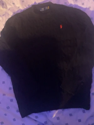 Svart kabelstickad tröja Polo Ralph Lauren - Kabelstickad svart tröja från Polo Ralph Lauren med klassisk röd logga. Gott använt men har inte några hål. Fraktar iväg samma dag som köps🚛🚛✅