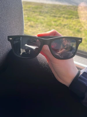 Svarta Ray-Ban Wayfarer solglasögon - Klassiska svarta Wayfarer solglasögon från Ray-Ban med ikonisk form och mörka glas. Snygg och tidlös design som passar till allt. Ray-Ban-loggan syns på sidan av bågen. Perfekta för soliga dagar.