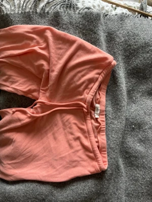 Persikofärgade mjukisbyxor från H&M - Mjukisbyxor i persikofärgad bomull från H&M med resår och dragsko i midjan. Byxorna har en avslappnad passform och är perfekta för chill dagar. Materialet är mjukt och lätt, vilket gör dem riktigt sköna att ha på sig.