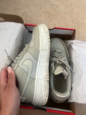 Nike Air Force 1 vita/ljus gröna sneakers - klassiska Nike Air Force 1 sneakers i läder med chunky sula och ikonisk swoosh på sidan, detaljer längs sulan. Skorna har snörning och perforeringar på tån för extra ventilation. Vara använt en månad. Bekväma inget slitage kan rengöras om sådant önskas. Köpt i butik (ej orginal kartong i bilden) storlek 39. Pris är disskuterbart!