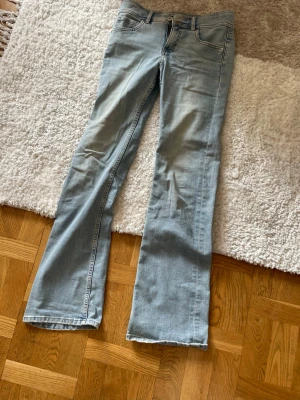 Ljusblå bootcut jeans med dubbelknapp - Ljusblå jeans med bootcut passform och dubbelknapp framtill. Klassisk femficksdesign och slitna detaljer vid knapparna. Materialet är denim med tydliga sömmar och dragkedja. Det gul liknande på jeansen är urblekt från början k butik! Varför jag säljer dom är för att dom är för små. Perfekt för dig som gillar en avslappnad och trendig look
