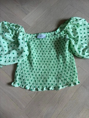 Grön prickig blus från grunt - Säljer en ljusgrön blus från grunt med gröna prickar och puffiga korta ärmar. Blusen har smockad kropp och volangkant nertill, vilket ger en söt och trendig look. Perfekt för dig som gillar färg och mönster! Storleken är L men den är kort och stretchig så jag skulle säga ungefär storleken S.