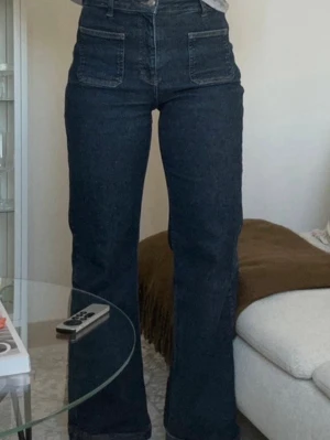 Mörkblå high waist jeans med fickor - Säljer ett par mörkblå jeans med hög midja och raka ben. Jeansen har stora fyrkantiga fickor framtill och klassiska bakfickor. Materialet är kraftig denim och passformen är relaxed med lätt utsvängda ben. Perfekta till en trendig vardagslook.