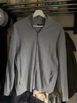 Grå ziptröja från Massimo Dutti - Snygg grå ziptröja från Massimo Dutti i bomull. Tröjan har hel dragkedja framtill, ståkrage och två fickor på sidorna. Perfekt för lager på lager och enkel att matcha med olika outfits.