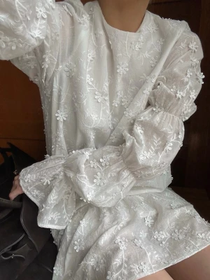 Studentklänning  - Vit blommig klänning med volang. Klänningen har långärmade puffärmar och är tillverkad i ett lätt, luftigt material. Perfekt för sommarens alla tillfällen och ger en söt och trendig look.  Helt ny med prislapp