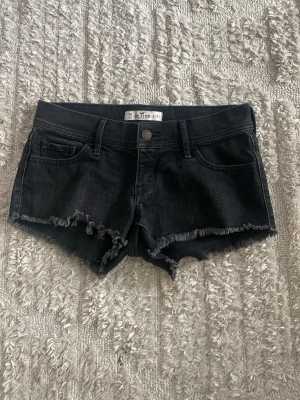 Svarta jeansshorts från Hollister - Snygga svarta jeansshorts från Hollister med klassisk knapp framtill och diskret logga. Perfekta för en avslappnad stil och lätta att matcha med olika toppar. Modellen har en smal passform och är tillverkad i bomull.  super bra skick! 