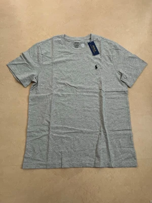 Ralph lauren T-shirt grå storlek large  - Ny Ralph Lauren t-shirt med klassisk passform. Perfekt basplagg till sommaren.  Oanvänd Väldigt populär modell Enkel att matcha  Skickas snabbt 📦 Rabatt vid köp av flera.