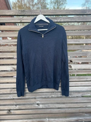 Mörkblå tröja med halv dragkedja - Mörkblå långärmad tröja från Jack & Jones med hög krage och halv dragkedja framtill. Tröjan har ribbade muddar vid ärmslut och nederkant, vilket ger en snygg och stilren look. Perfekt för lager-på-lager och passar till många outfits.