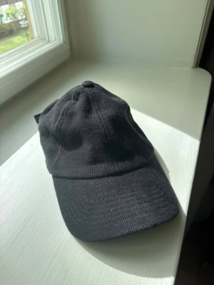 Svart klassisk keps i bomull - En stilren svart keps med böjd skärm och justerbar rem baktill. Kepsen är tillverkad i mjuk bomull och har en enkel, tidlös design utan synligt märke. Perfekt för en clean och avslappnad look.